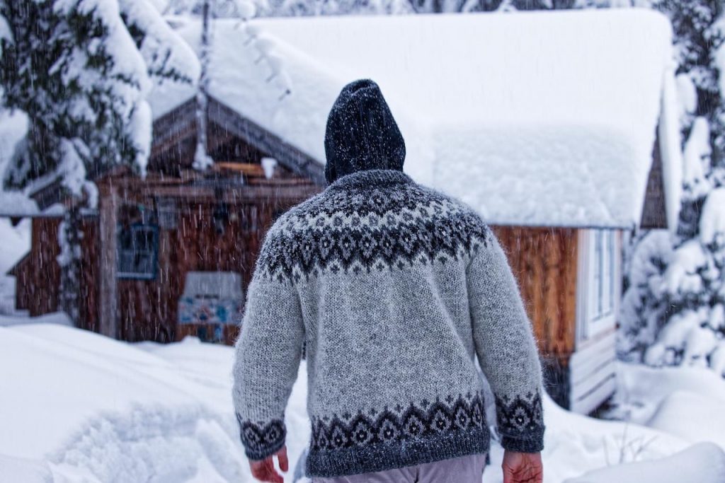 Person wearing a traditional wool yoke jumper walking through deep snow in northern Sweden during winter snowfall.