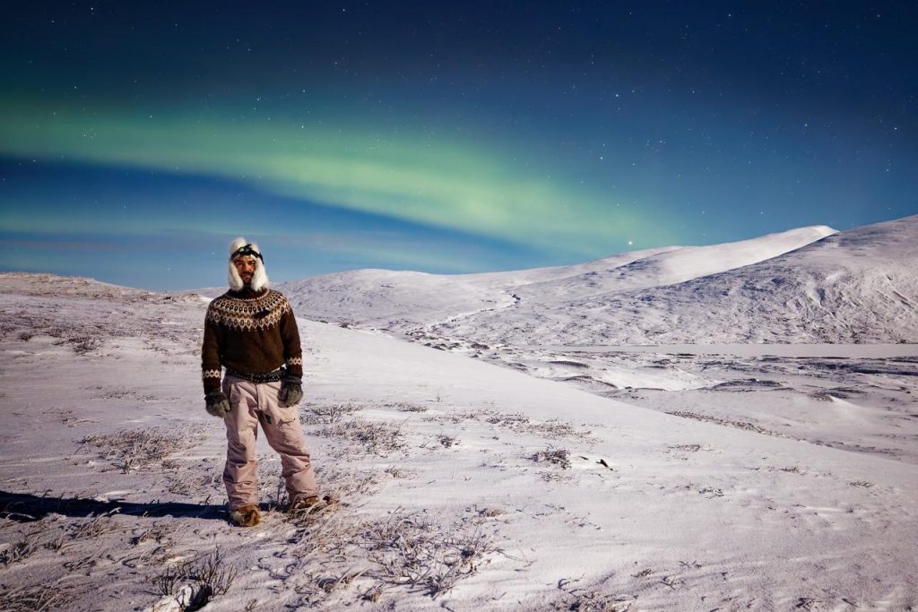 Person wearing a traditional wool yoke jumper standing in a snowy northern Swedish landscape beneath the Northern Lights at night.